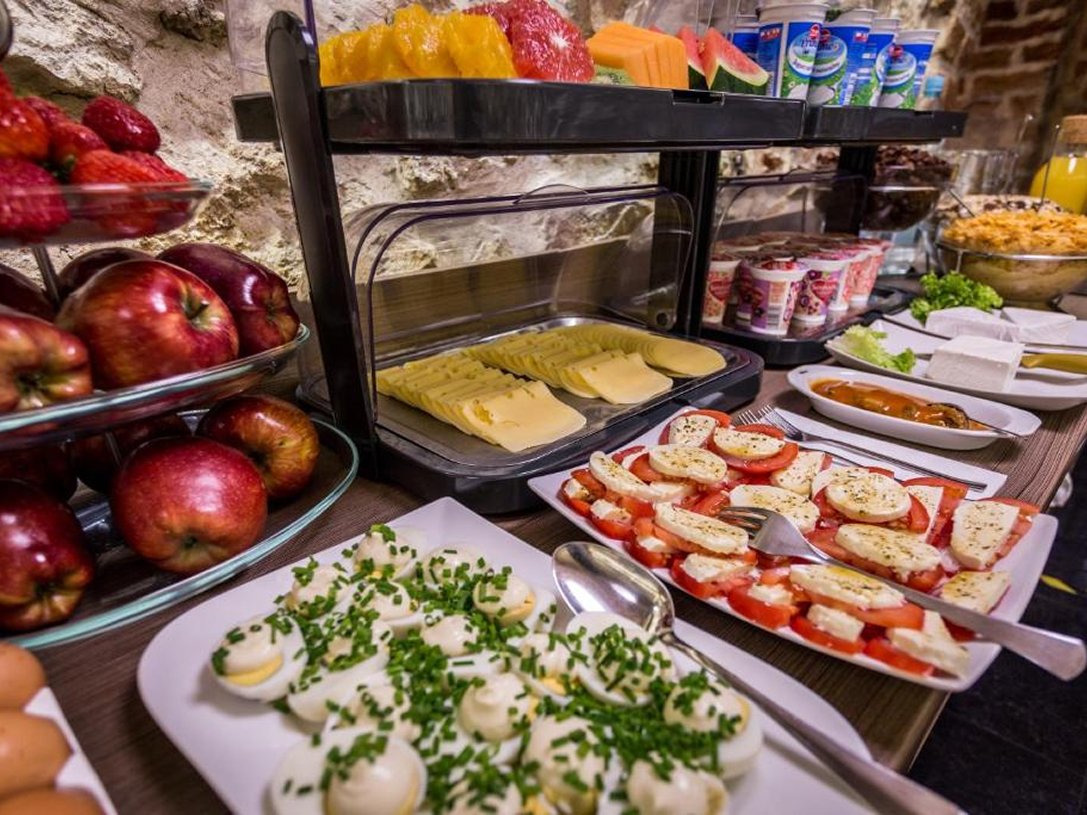 Stół z różnorodnym śniadaniem obejmującym jajka faszerowane posypane szczypiorkiem, plastry sera, sałatkę z pomidorów i sera, jabłka, truskawki oraz jogurty.