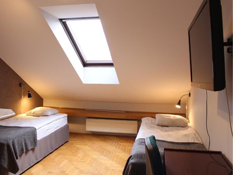 Pokój poddaszowy z dwoma pojedynczymi łóżkami, oknem dachowym, telewizorem na ścianie i drewnianą podłogą.