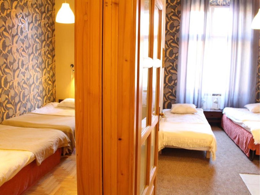 Pokój z podwójnym łóżkiem po lewej stronie oraz dwoma pojedynczymi łóżkami po prawej stronie, dekorowane tapetą i zasłonami.