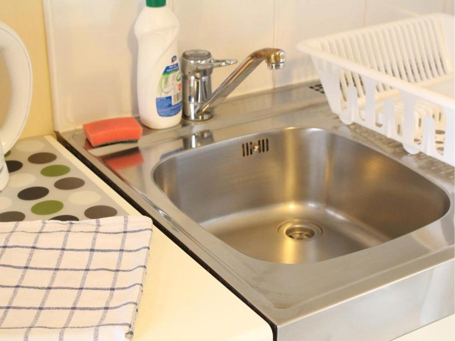 Kuchenny zlew ze stali nierdzewnej z kranem, plastikową suszarką na naczynia, gąbką do mycia i butelką detergentu.