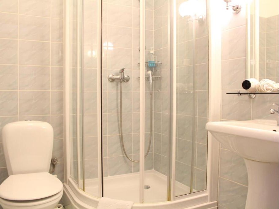 Łazienka z prysznicem z drzwiami przesuwnymi, toaletą i umywalką na tle jasnoszarych płytek.