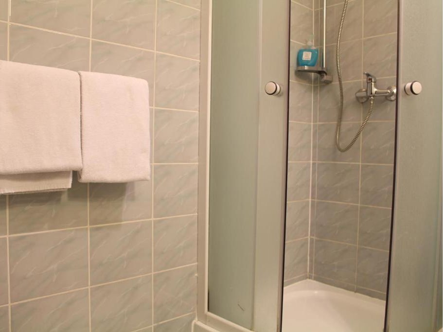 Łazienka z białą umywalką, półką z suszarką do włosów i mydłem w płynie, prysznicem oraz ręcznikiem na wieszaku.