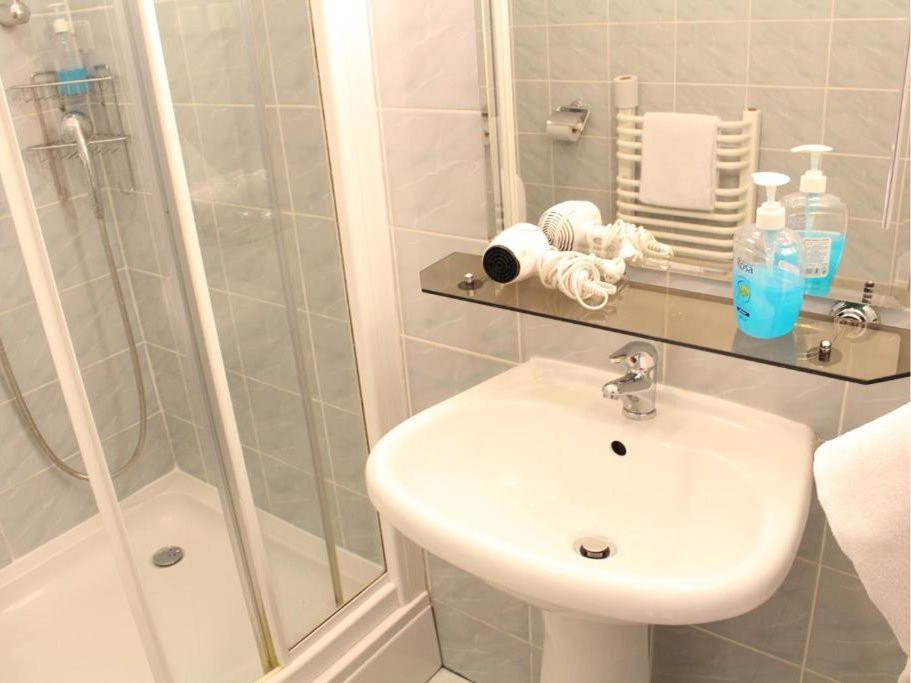 Kuchenny zlew ze stali nierdzewnej z kranem, plastikową suszarką na naczynia, gąbką do mycia i butelką detergentu.